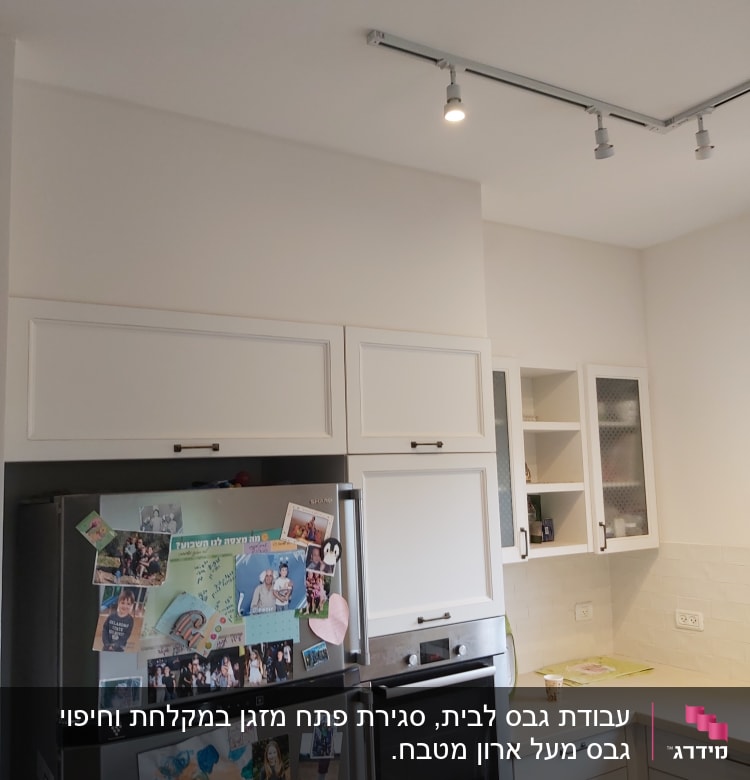 מטבח עם ארונות לבנים ותאורה עליונה